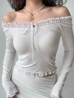 Woman wearing a white off-the-shoulder ribbed knit top with ruffled trim and tie front, paired with a white skirt.