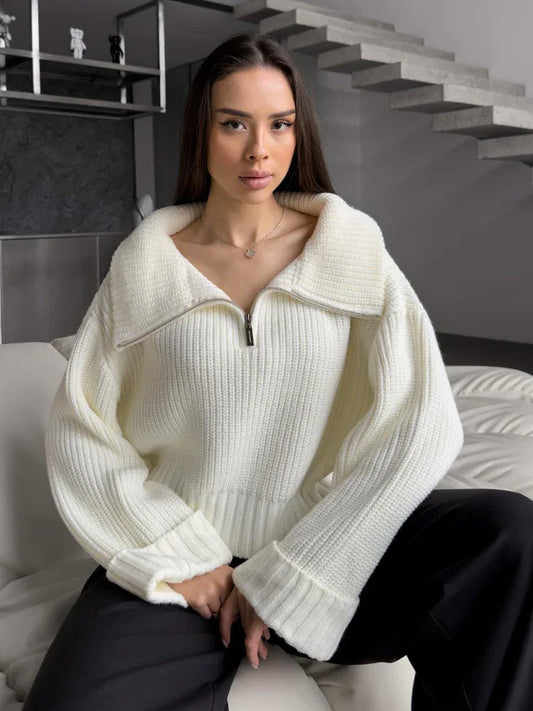 Woman wearing a cream-colored oversized knit sweater with a half-zip neckline and wide sleeves, sitting on a couch.
