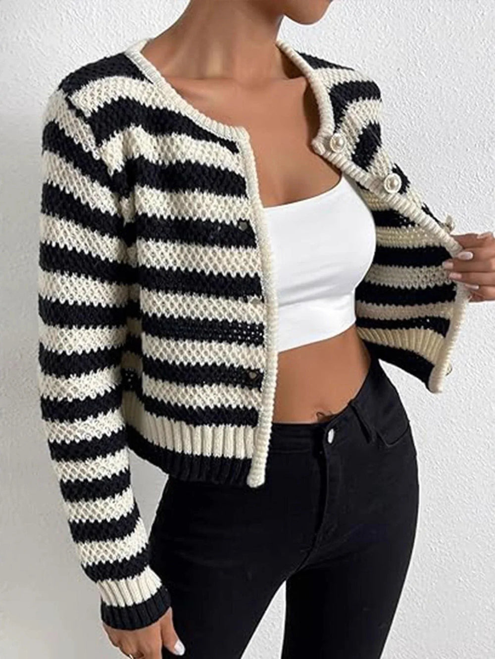 Close-up of a woman wearing a black and white striped cropped knit cardigan and black jeans, showing the texture and button details.
