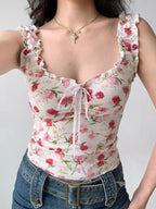 Detail of the neckline and bodice of a white floral print top with ruffles and a pink ribbon tie.