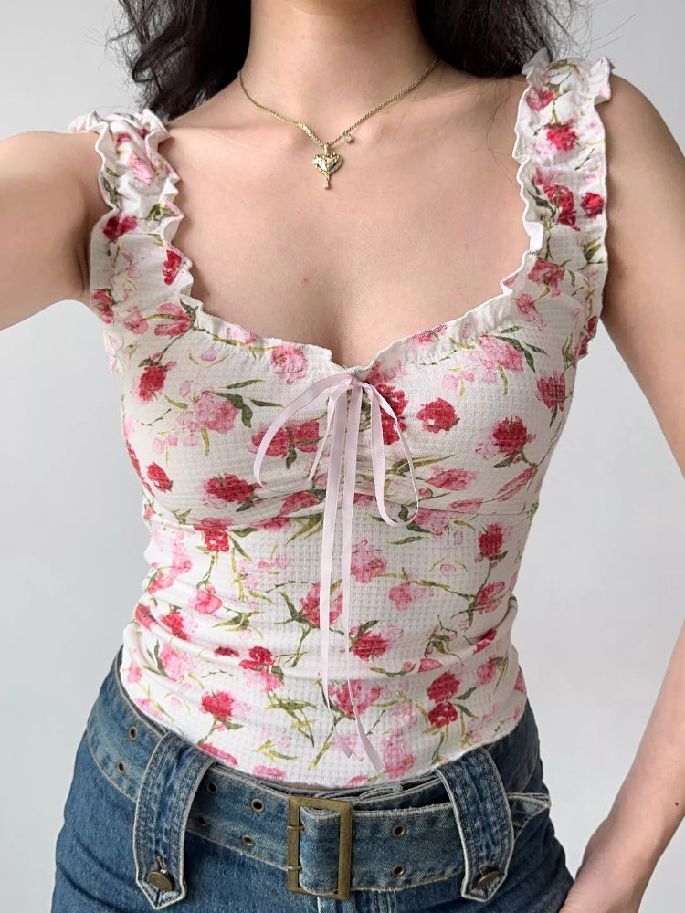 Detail of the neckline and bodice of a white floral print top with ruffles and a pink ribbon tie.
