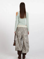 Back view of a woman wearing a mint green long-sleeved shirt with an asymmetrical neckline and a cut-out shoulder, paired with wide-leg leopard print pants, a striped belt, and brown boots.