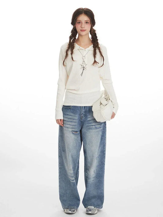 Woman wearing a white ribbed knit long-sleeve shirt with a collared neckline and a star pendant necklace, paired with distressed wide-leg blue jeans and a white handbag.