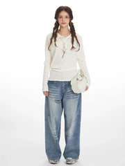 Woman wearing a white ribbed knit long-sleeve shirt with a collared neckline and a star pendant necklace, paired with distressed wide-leg blue jeans and a white handbag.