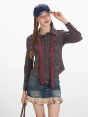 Three-quarter front view of a woman adjusting her baseball cap, wearing a plaid button-down shirt, denim mini skirt with faux fur trim, and a tie.