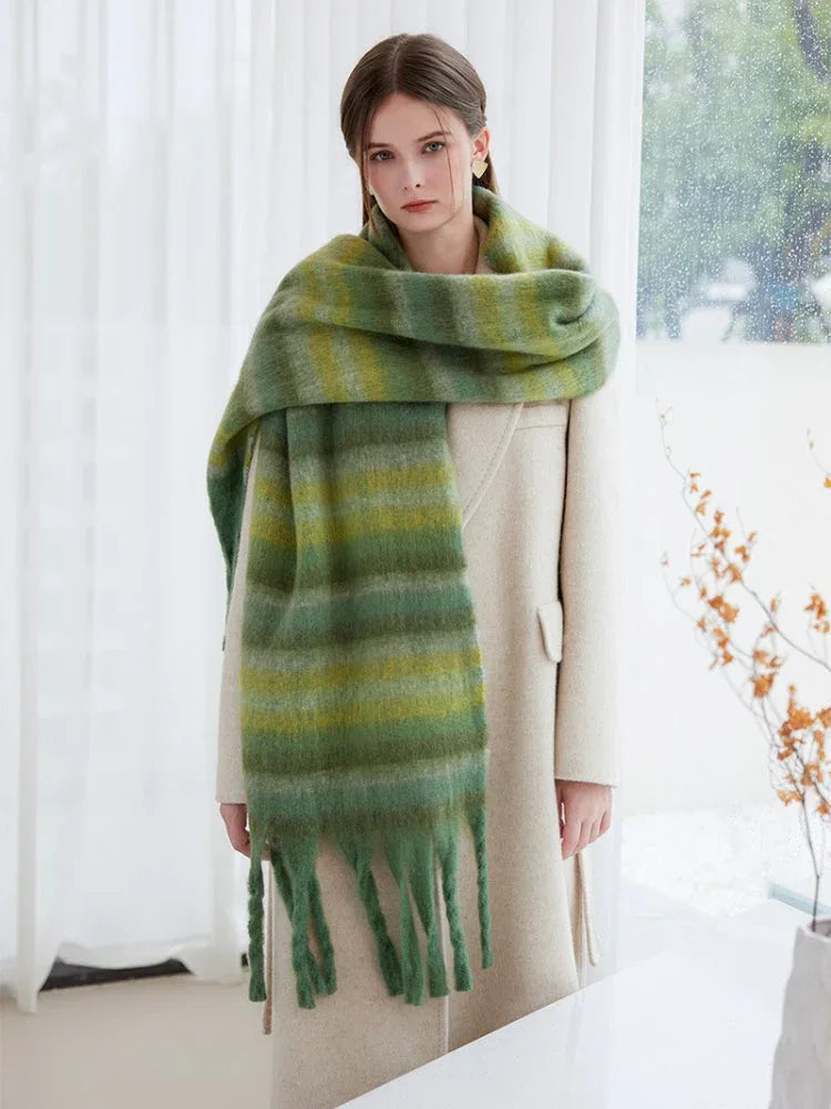 Full body shot of a woman in a cream coat and a green striped scarf with fringe.