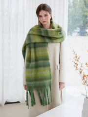 Full body shot of a woman in a cream coat and a green striped scarf with fringe.