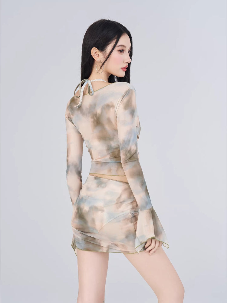 Rear view of a woman wearing a sheer mesh abstract print two-piece set, showing the back of the long-sleeve top and the ruched skirt.