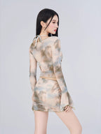 Rear view of a woman wearing a sheer mesh abstract print two-piece set, showing the back of the long-sleeve top and the ruched skirt.