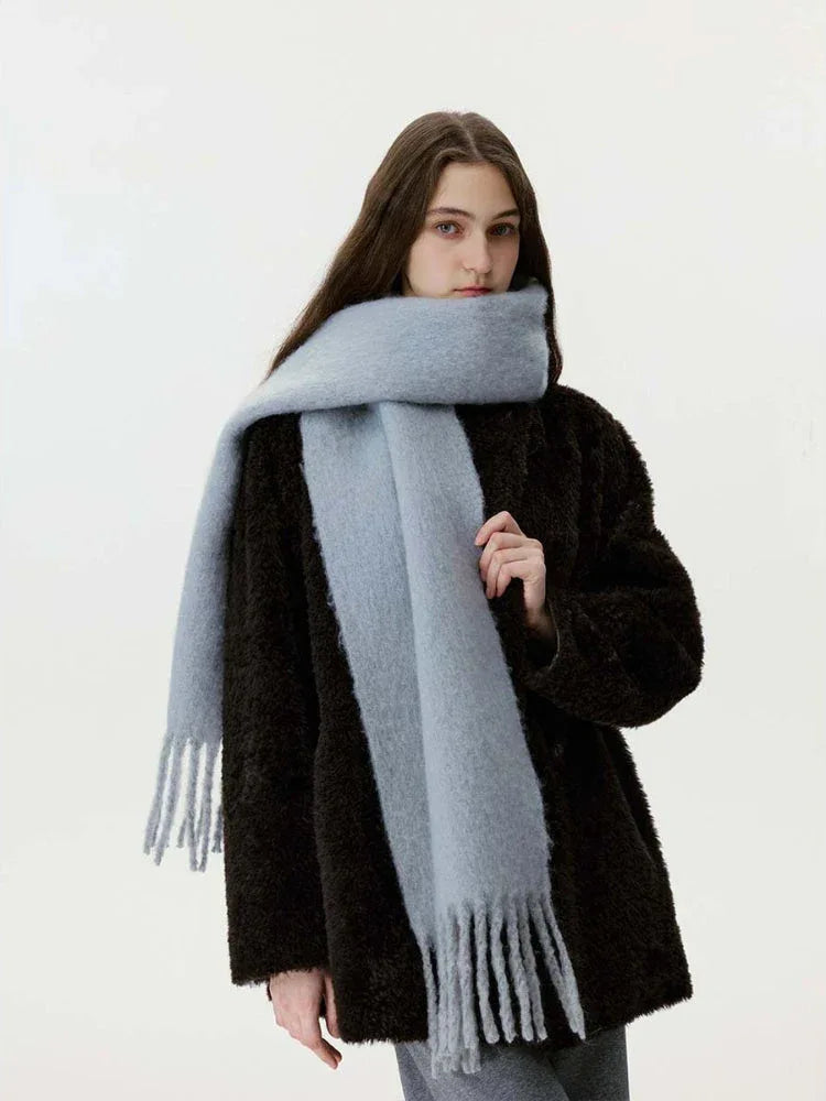 Woman wearing a black faux fur coat and a light blue fuzzy scarf with fringe.