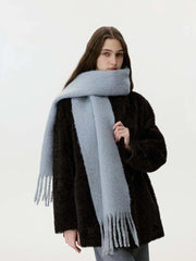Woman wearing a black faux fur coat and a light blue fuzzy scarf with fringe.