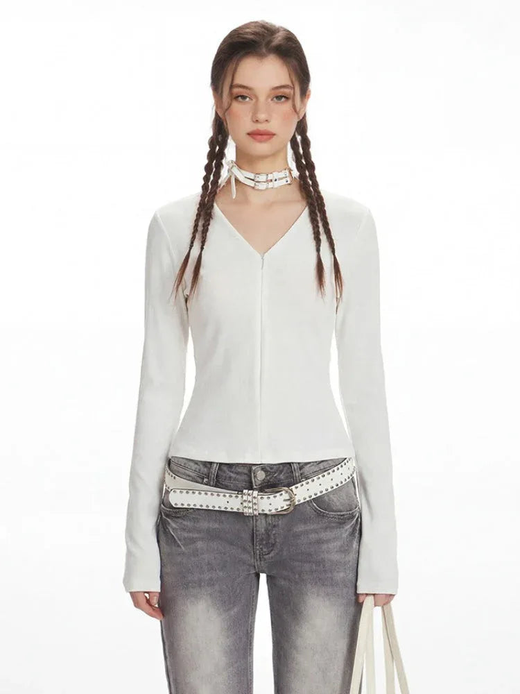 Close-up of the model's upper body, showing the white long-sleeved ribbed V-neck top and the white studded belt.