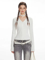 Close-up of the model's upper body, showing the white long-sleeved ribbed V-neck top and the white studded belt.