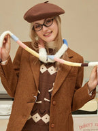 Woman in a brown tweed blazer and argyle sweater, holding a colorful fuzzy scarf.