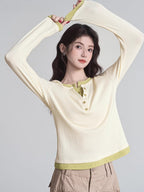 Woman in a cream long-sleeved shirt with green trim and buttons, raising her arms.