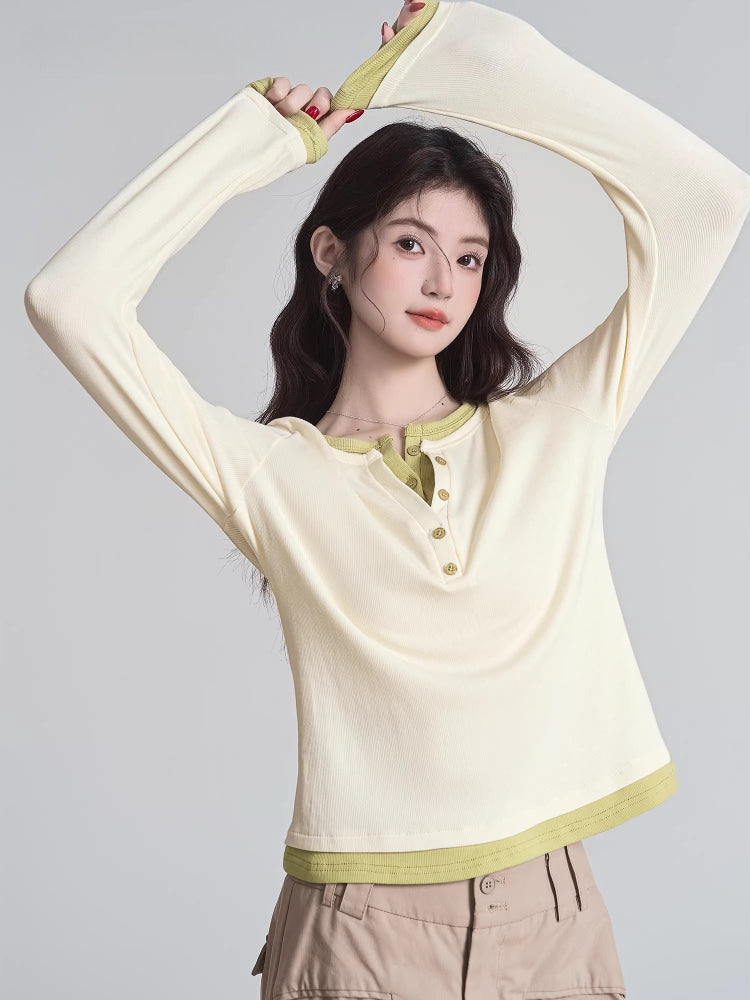 Woman in a cream long-sleeved shirt with green trim and buttons, raising her arms.