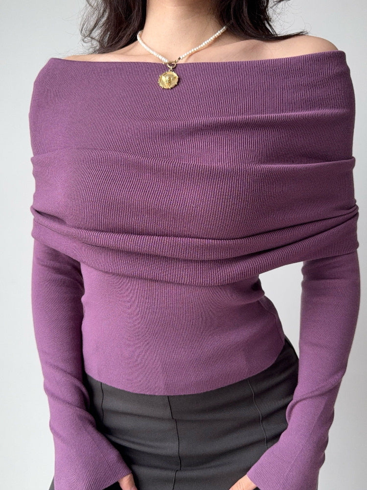 Front view of a woman wearing a purple off-the-shoulder knit top with a draped neckline and long sleeves.