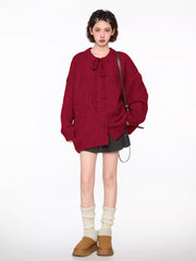 Full body shot of a woman wearing a red knit cardigan with tie neck and buttons, grey pleated skirt, brown crossbody bag, and white leg warmers.