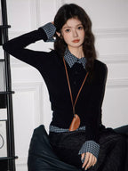 Model in a black long-sleeved top with checkered details, dark wash wide-leg jeans, and a brown bag, posing with one hand on her head.