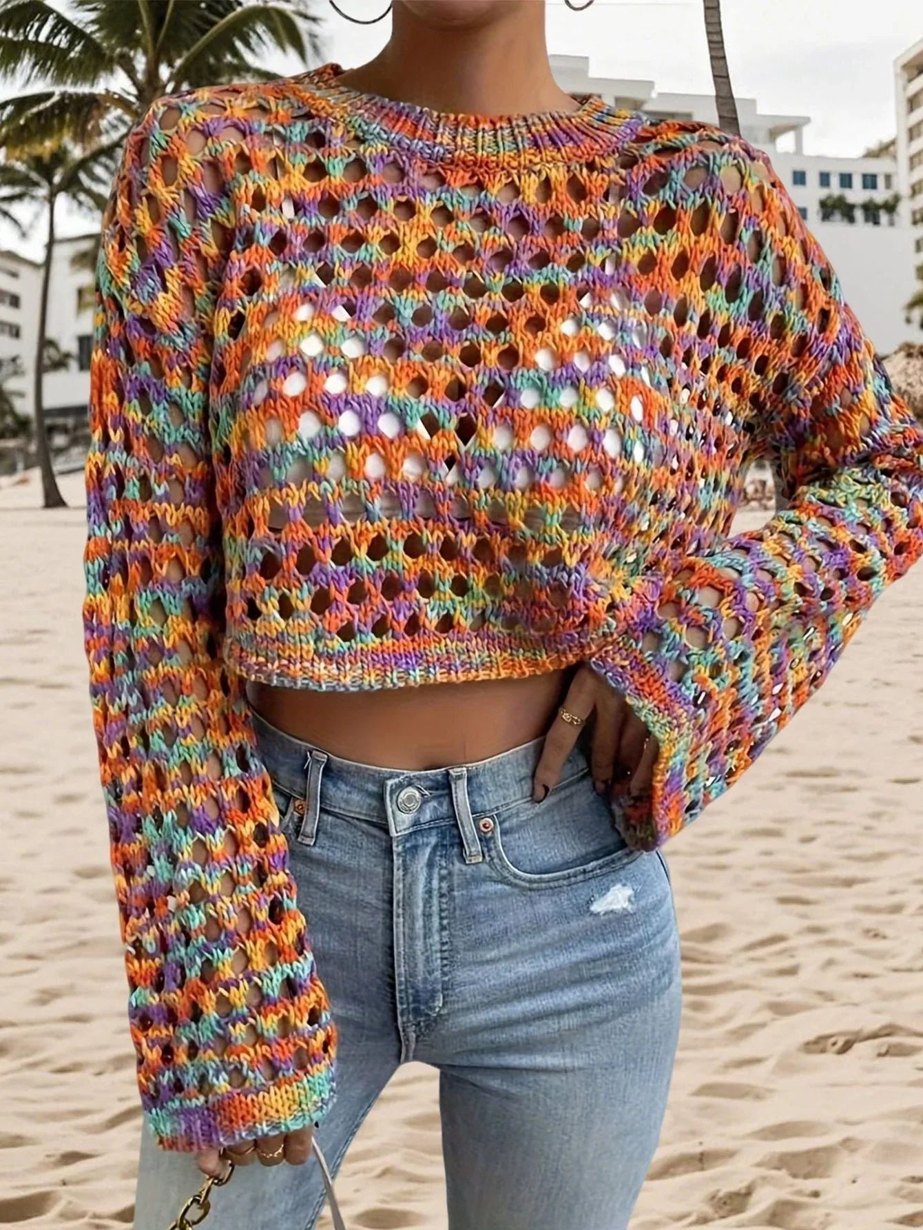 Front close-up of a woman's torso wearing a multicolored open-knit cropped sweater and light-wash denim jeans.