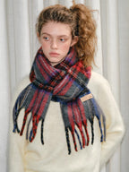 Model wearing a cream-colored sweater and a red, blue, and gray tartan plaid scarf with fringes.