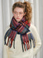 Model wearing a cream-colored sweater and a red, blue, and gray tartan plaid scarf with fringes.