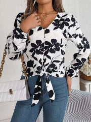 Woman wearing a black and white floral print long sleeve blouse with a front tie detail and blue jeans, holding a white handbag, front view