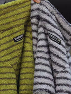 Close-up of two dog sweaters, one lime green and one gray and white, both with striped patterns and brand tags