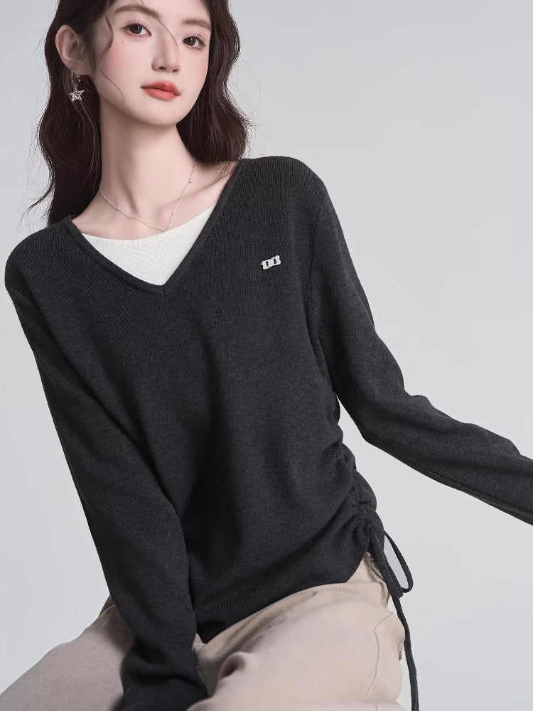 Close-up of a woman wearing a dark grey v-neck sweater over a white layer, showcasing the ruched side detail.