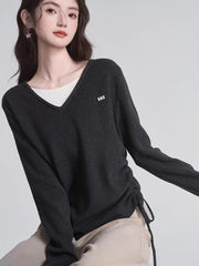 Close-up of a woman wearing a dark grey v-neck sweater over a white layer, showcasing the ruched side detail.