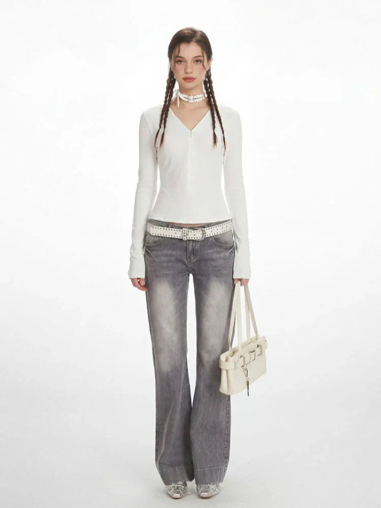 Model wearing a white long-sleeved ribbed V-neck top with grey flared jeans, a white studded belt, a white choker, and a white shoulder bag.