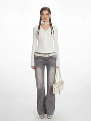 Model wearing a white long-sleeved ribbed V-neck top with grey flared jeans, a white studded belt, a white choker, and a white shoulder bag.