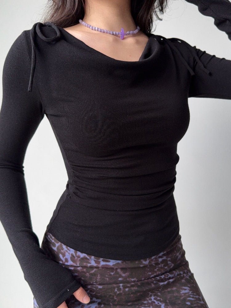 Model wearing a black long-sleeve top with a draped neckline and ruched sides, paired with a patterned skirt.