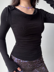 Model wearing a black long-sleeve top with a draped neckline and ruched sides, paired with a patterned skirt.
