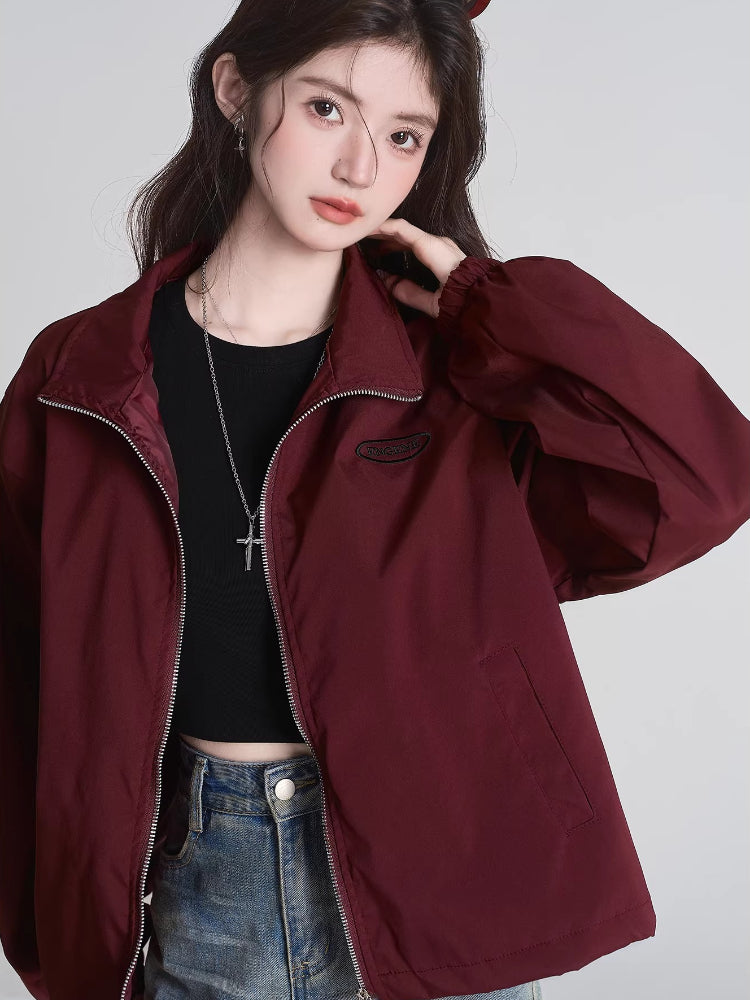 Close-up of the burgundy bomber jacket showing the zipper, collar, and embroidered logo.
