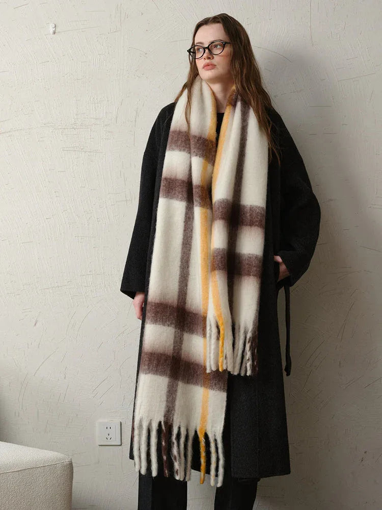 Full body shot of a woman wearing a long dark coat and a large plaid scarf with white, brown, and yellow stripes.