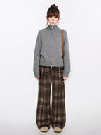 Full body shot of a woman in a grey zip-up knit sweater and brown plaid wide-leg pants.