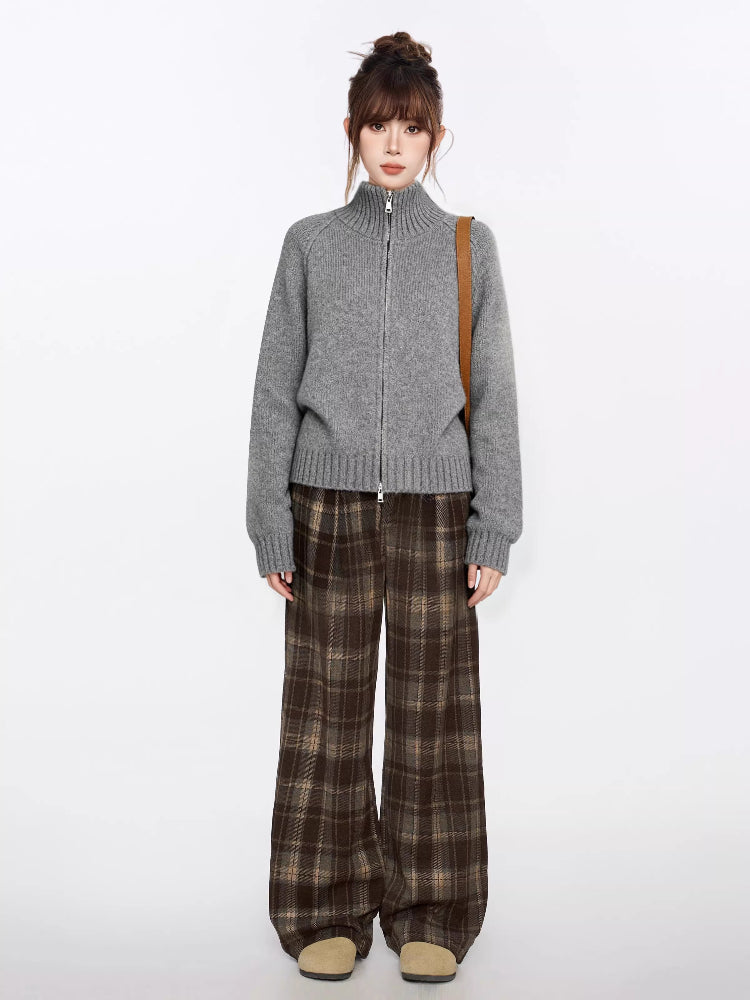 Full body shot of a woman in a grey zip-up knit sweater and brown plaid wide-leg pants.
