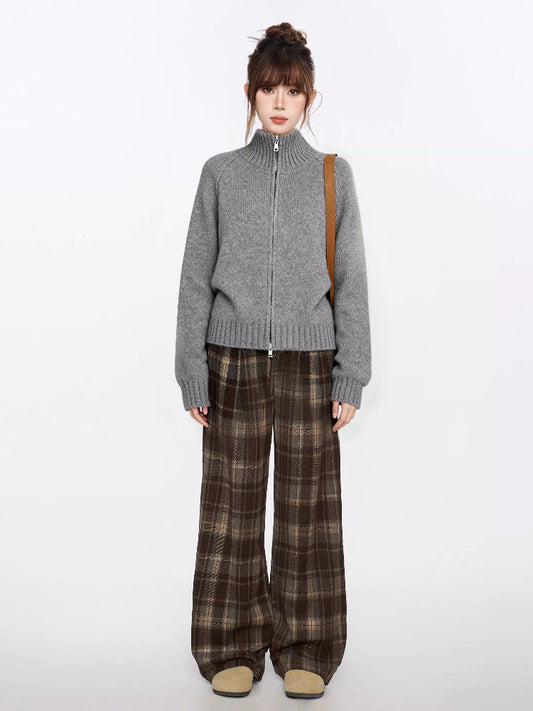 Full body shot of a woman in a grey zip-up knit sweater and brown plaid wide-leg pants.