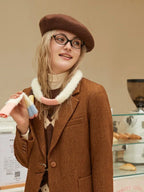 Close-up of a woman wearing a brown tweed blazer, argyle knit sweater, and fuzzy striped scarf, smiling and holding the scarf.