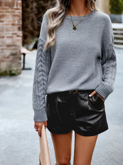 Side view of a woman wearing a grey knit sweater with cable knit sleeves and black shorts.