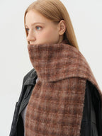 Detailed view of a woman wearing a brown plaid scarf around her neck, layered over a black leather jacket.