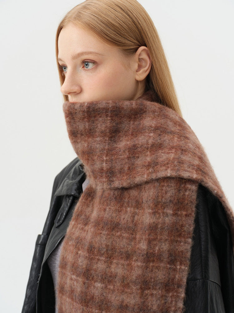 Detailed view of a woman wearing a brown plaid scarf around her neck, layered over a black leather jacket.