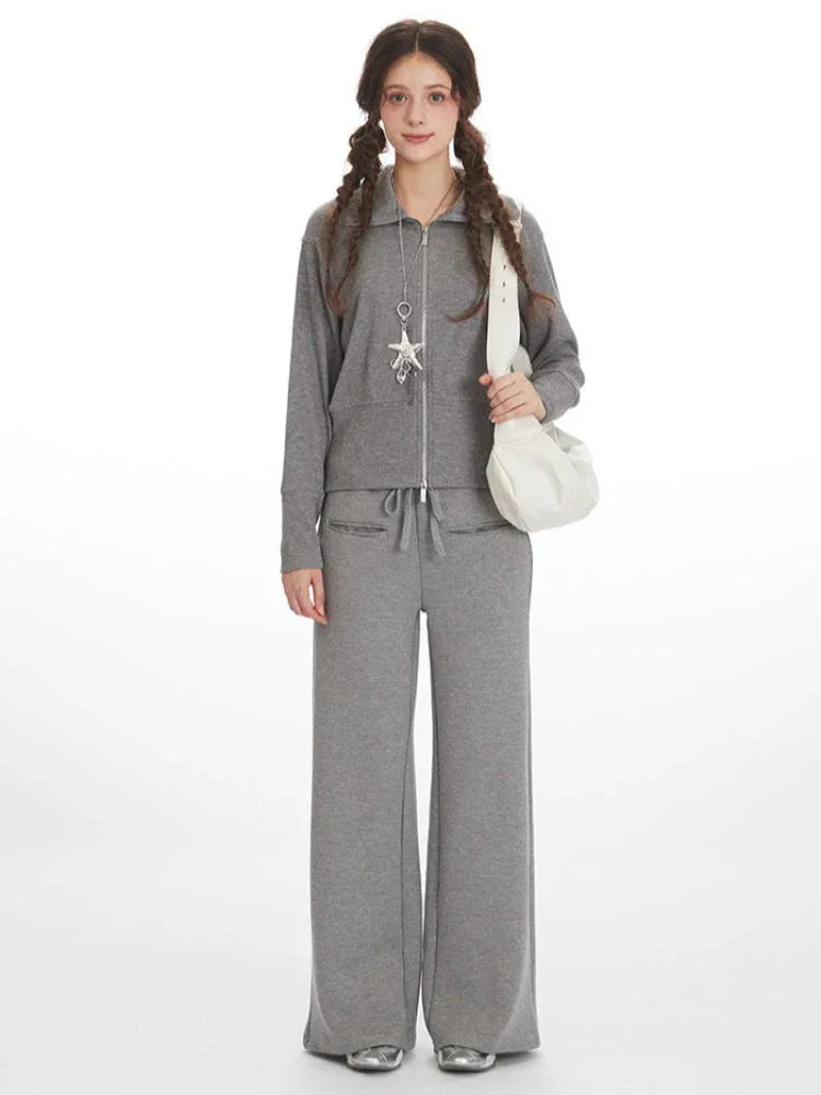 Woman wearing a grey knit zip-up jacket and wide-leg pants with a white shoulder bag. Main image