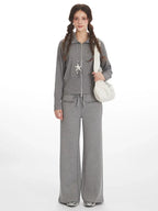 Woman wearing a grey knit zip-up jacket and wide-leg pants with a white shoulder bag.