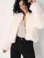 Woman with curly hair smiling, wearing a white faux fur jacket over a sparkly top and black jeans.
