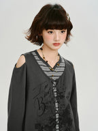 Close-up of the model's face and upper body, showcasing the layered grey top with graphic print and necklace.