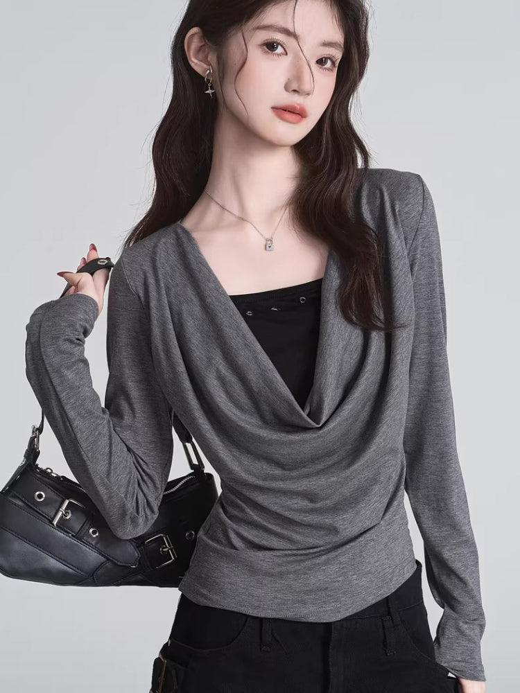 Woman wearing a grey draped long-sleeve top over a black camisole, paired with black pants and a black handbag.