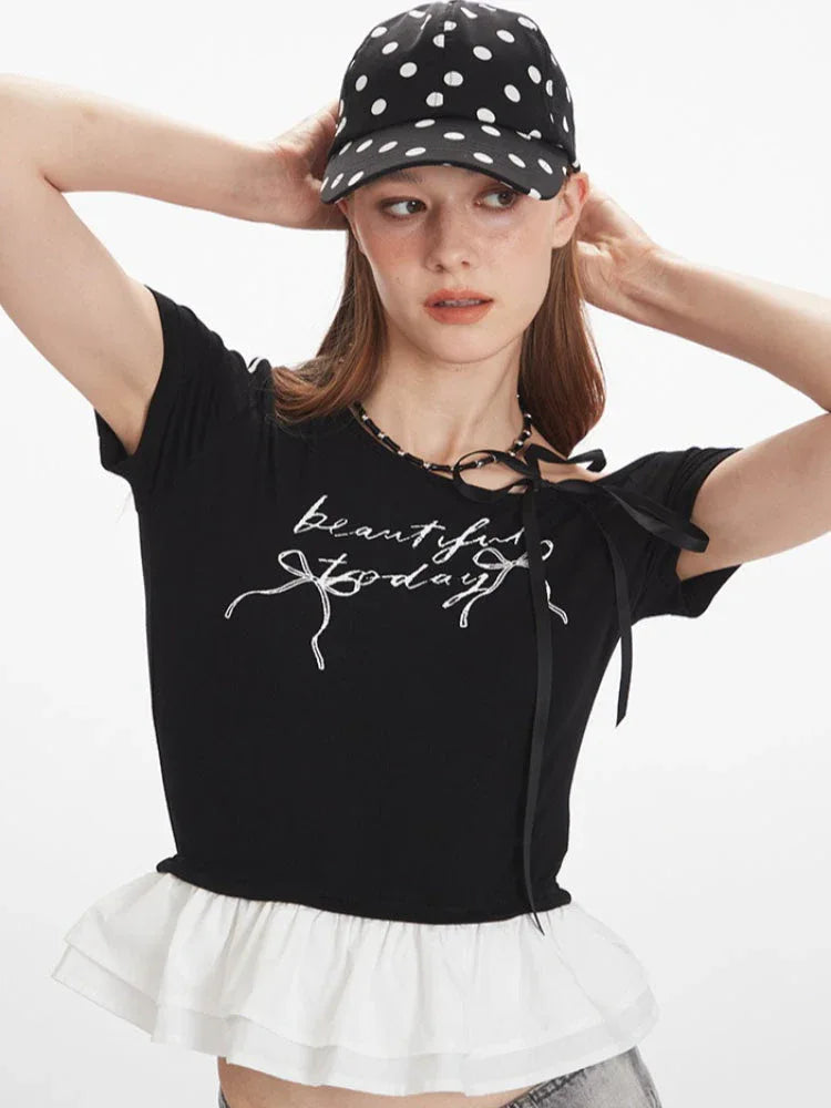 Front close-up of a woman's black off-the-shoulder top with graphic print and white ruffle trim.