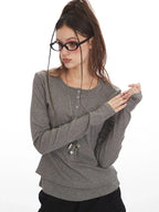 Close-up of a woman wearing a grey long-sleeved shirt, black cargo pants, and a star pendant necklace, posing with her hands.